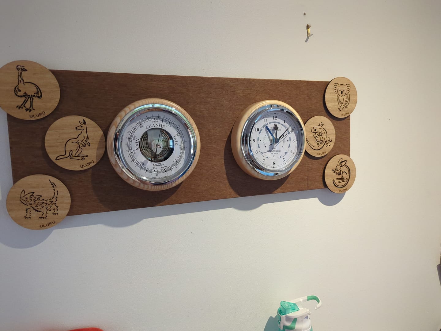 Wall-mounted German barometer and clock with wooden animal coasters, home weather station.
