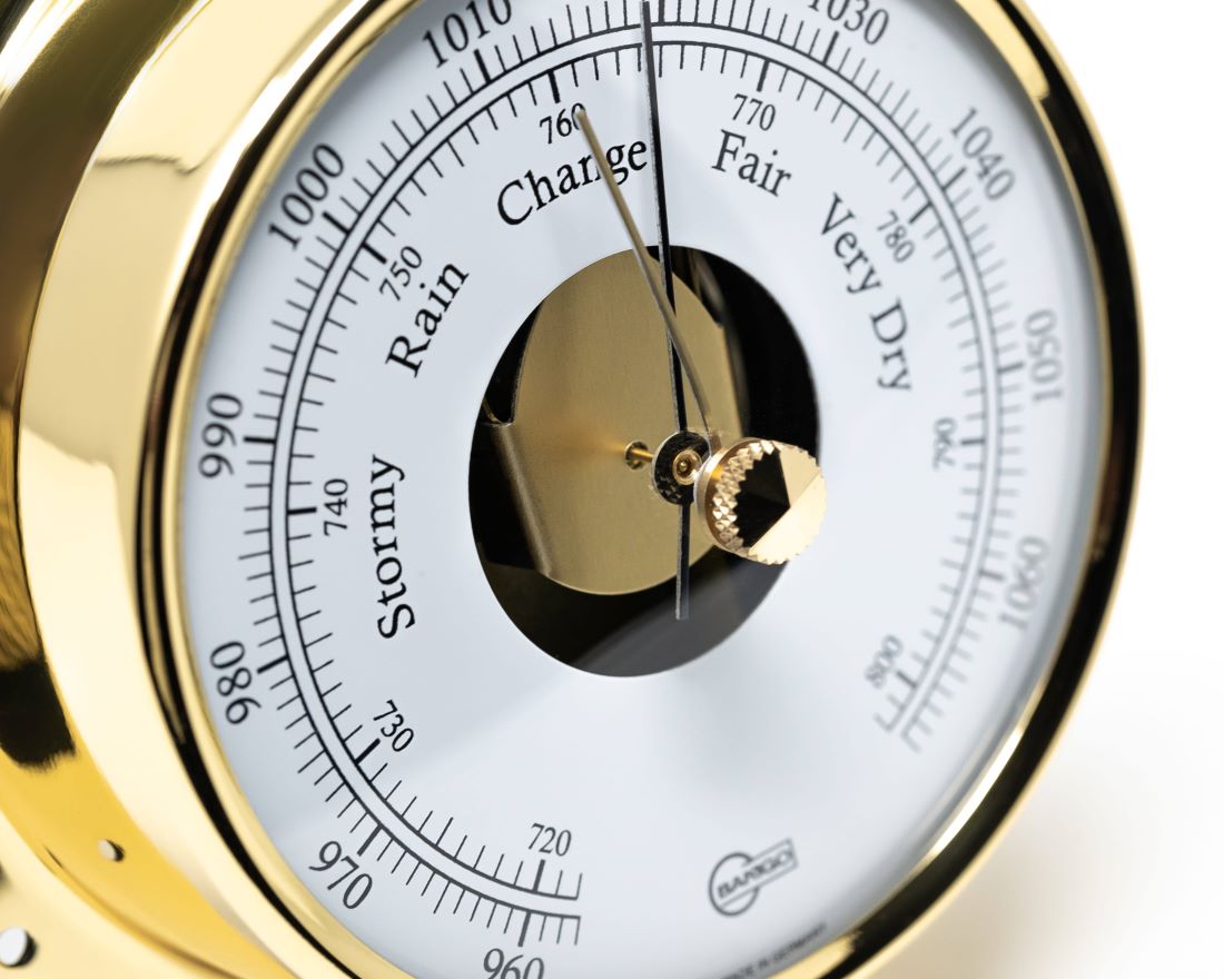 Close-up of a brass analog barometer with weather and pressure scale dial.