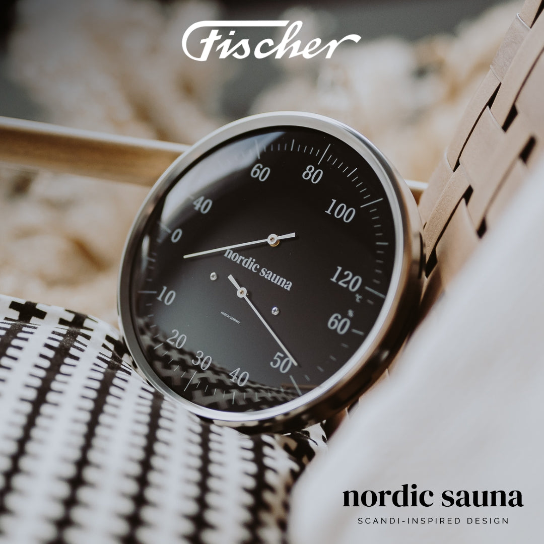 Black analog sauna thermometer with humidity dial, Nordic sauna design, on woven chair.