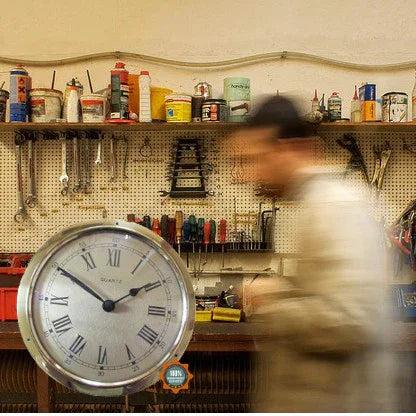 Wall clock with Roman numerals in workshop with tools and blurred person walking by