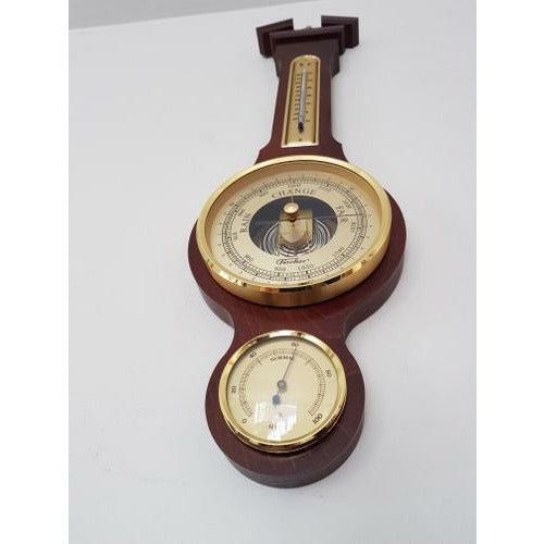 Man indoors looking at wall-mounted mahogany weather station barometer and hygrometer